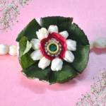 Eco-friendly floral rakhi with white jasmine buds, red rose center, green leaves, and jeweled centerpiece