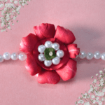 Eco-friendly rakhi featuring a red rose made of fresh petals with pearl-like center and green leaf, on a pearl bead strand