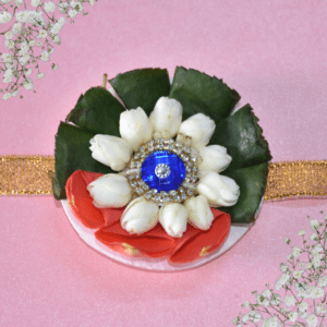 Eco-friendly rakhi featuring white jasmine buds, red rose petals, green leaves, and blue gemstone centerpiece on golden ribbon