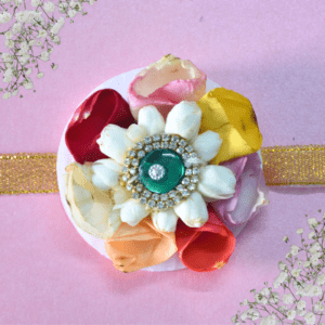 Eco-friendly rakhi featuring white jasmine center with emerald gemstone, surrounded by multicolored rose petals on golden ribbon