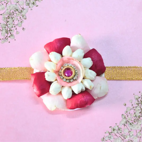 Eco-friendly rakhi featuring white jasmine buds, red and pink rose petals, with pink gemstone centerpiece on golden ribbon