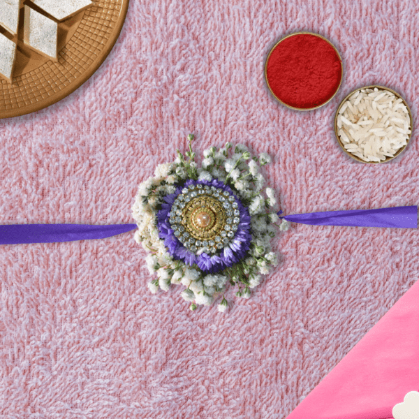 Eco-friendly floral Rakhi with gold and crystal centerpiece, purple asters, white baby's breath, and purple ribbon