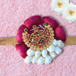 Eco-friendly rakhi with red rose petals, white jasmine buds, and ornate gold centerpiece on golden ribbon