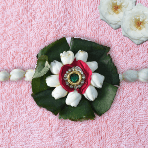 Eco-friendly floral rakhi with white jasmine buds, red rose center, green leaves, and jeweled centerpiece