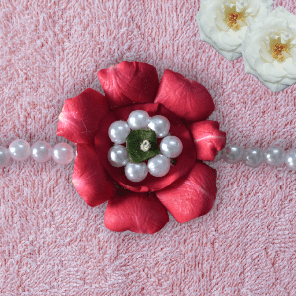 Eco-friendly rakhi featuring a red rose made of fresh petals with pearl-like center and green leaf, on a pearl bead strand