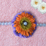 Handcrafted floral Rakhi with orange gerbera daisy, purple chrysanthemums, and pearl center