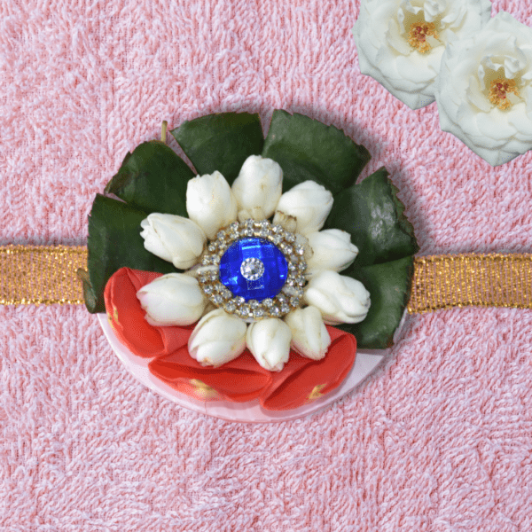 Eco-friendly rakhi featuring white jasmine buds, red rose petals, green leaves, and blue gemstone centerpiece on golden ribbon