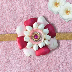 Eco-friendly rakhi featuring white jasmine buds, red and pink rose petals, with pink gemstone centerpiece on golden ribbon