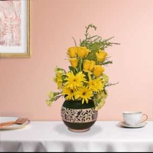 A bunch of yellow roses, yellow carnation, yellow gerbera, and green leaves beautifully arranged in a vase