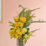 A bunch of yellow roses, yellow carnation, yellow gerbera, and green leaves beautifully arranged in a vase