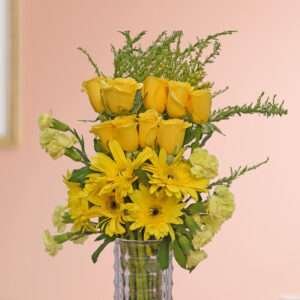 A bunch of yellow roses, yellow carnation, yellow gerbera, and green leaves beautifully arranged in a vase