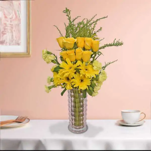 A bunch of yellow roses, yellow carnation, yellow gerbera, and green leaves beautifully arranged in a vase