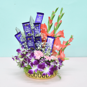 Luxurious flower bouquet with purple orchids, pink carnations, coral gladioli, and Cadbury Dairy Milk chocolates in a golden basket