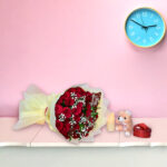 A bouquet of fresh red roses with baby's breath wrapped in cream paper, displayed against a pink background.