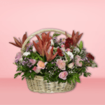 Colorful flower basket arrangement with orange lilies, pink roses, red carnations, and purple flowers in a wicker basket on pink background