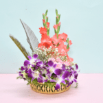 Tropical flower basket with coral gladioli, purple orchids, pink carnations, and silver feathers in a golden container