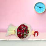 A bouquet of fresh red roses with baby's breath wrapped in cream paper, displayed against a pink background.