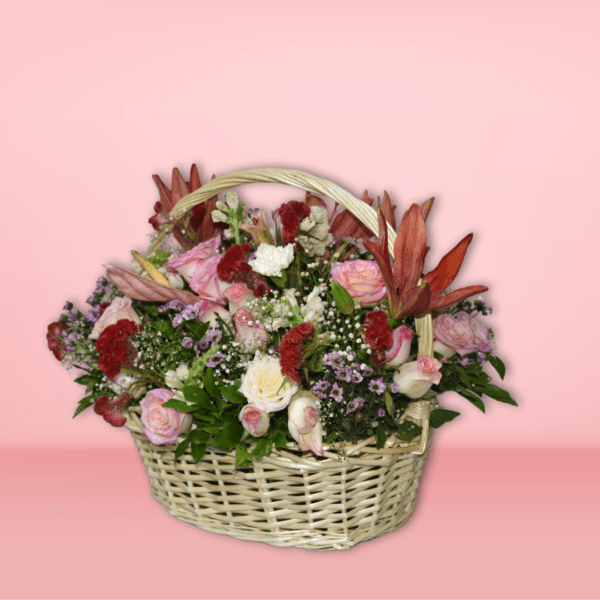 Colorful flower basket arrangement with orange lilies, pink roses, red carnations, and purple flowers in a wicker basket on pink background