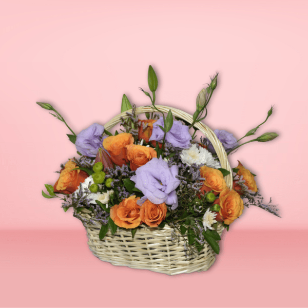 Colorful flower basket arrangement with orange roses, lavender lisianthus, white chrysanthemums, and green accents in a wicker basket on pink background