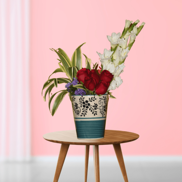 Elegant floral arrangement with red roses and white gladioli in decorative vase on wooden table, pink background