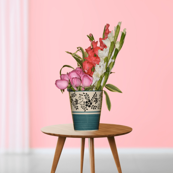 Colorful flower arrangement with pink roses and gladioli in decorative vase on wooden table, pink background