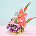 Tropical flower basket with coral gladioli, purple orchids, pink carnations, and silver feathers in a golden container