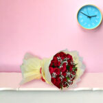 A bouquet of fresh red roses with baby's breath wrapped in cream paper, displayed against a pink background.