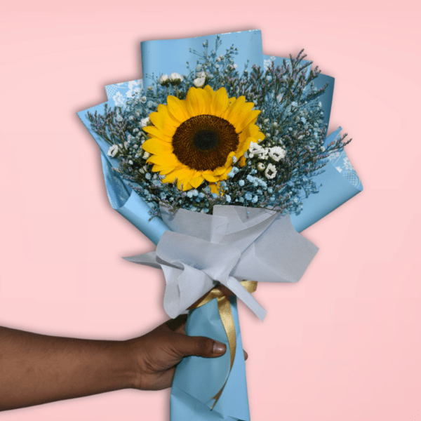 A beautiful bouquet featuring a large, vibrant sunflower surrounded by delicate baby's breath and greenery, wrapped in soft blue paper and tied with a shimmering gold ribbon.