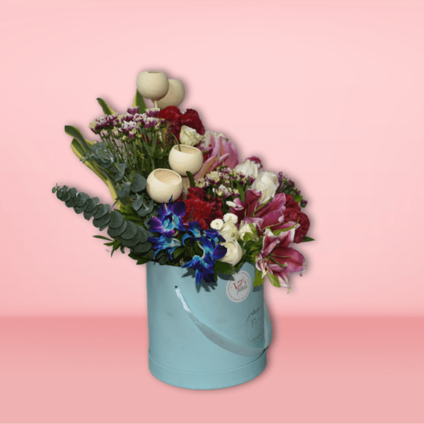 A beautiful floral bouquet featuring a variety of vibrant blooms, including red carnations, pink lilies, purple statice, and white tulips, presented in a charming turquoise vase