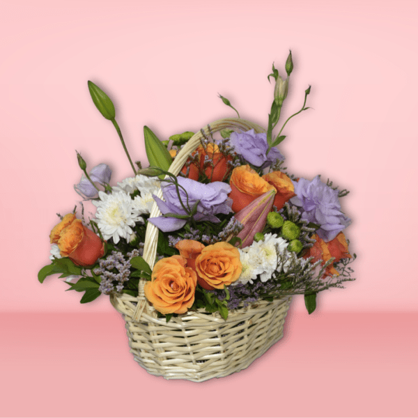 Colorful flower basket arrangement with orange roses, lavender lisianthus, white chrysanthemums, and green accents in a wicker basket on pink background