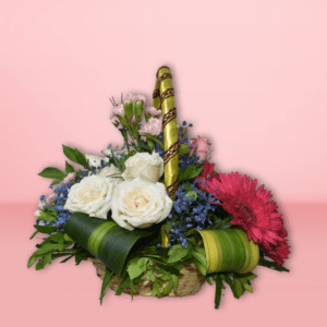 Flower basket with red gerberas, pink roses, white carnations, and Ferrero Rocher chocolates on a pink background.