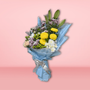 Mixed flower bouquet with yellow chrysanthemums, peach roses, white and purple carnations, wrapped in blue paper on a pink background.