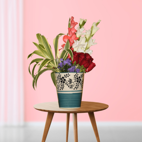 Elegant floral arrangement with red roses and white gladioli in decorative vase on wooden table, pink background