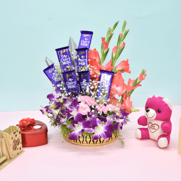 Luxurious flower bouquet with purple orchids, pink carnations, coral gladioli, and Cadbury Dairy Milk chocolates in a golden basket