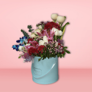 A beautiful floral bouquet featuring a variety of vibrant blooms, including red carnations, pink lilies, purple statice, and white tulips, presented in a charming turquoise vase