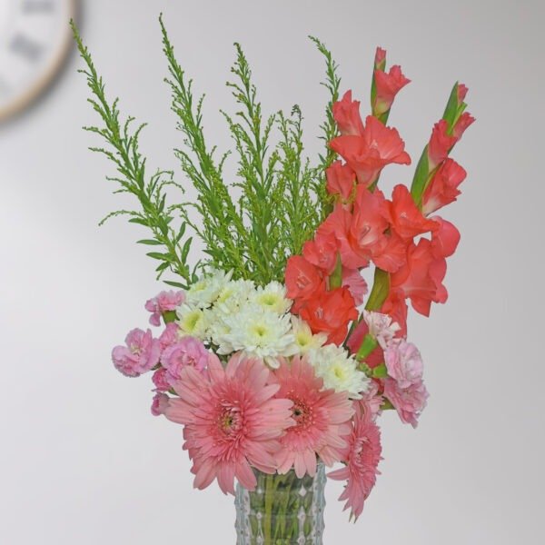 A mixed flower bouquet with red gladiolus, pink carnations, white chrysanthemums, and pink gerbera, arranged in a glass vase.