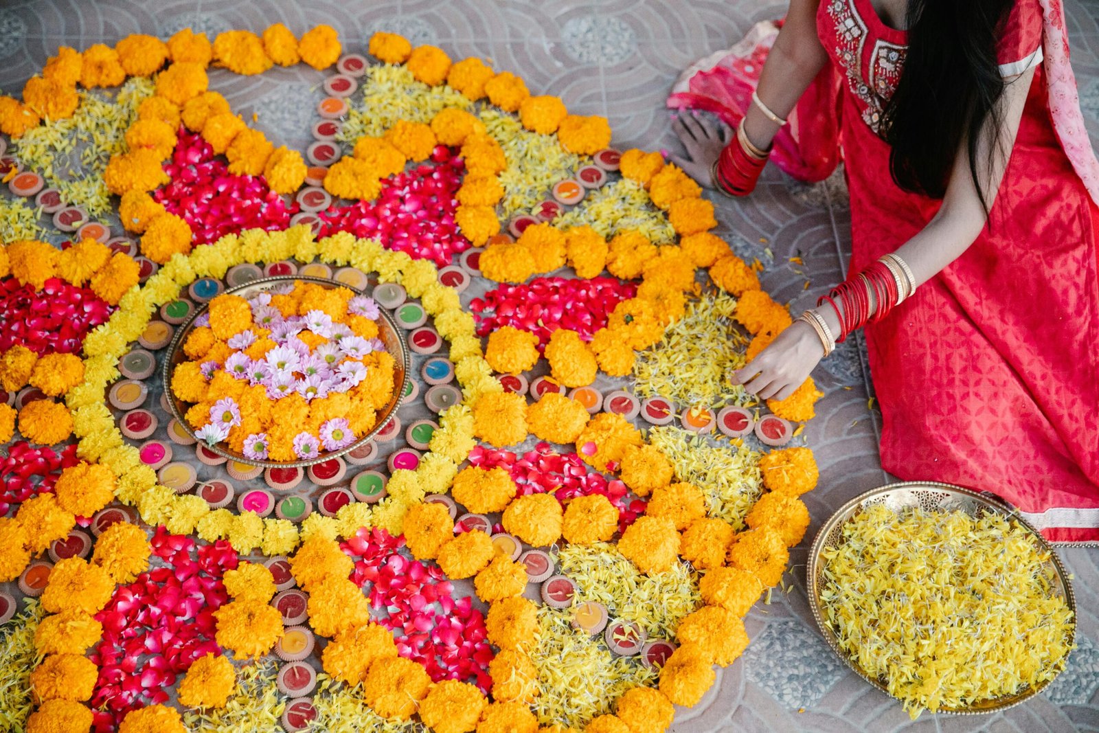 A girl making a beautiful pookkalam with rose petals, marigold and chrysanthemum 
