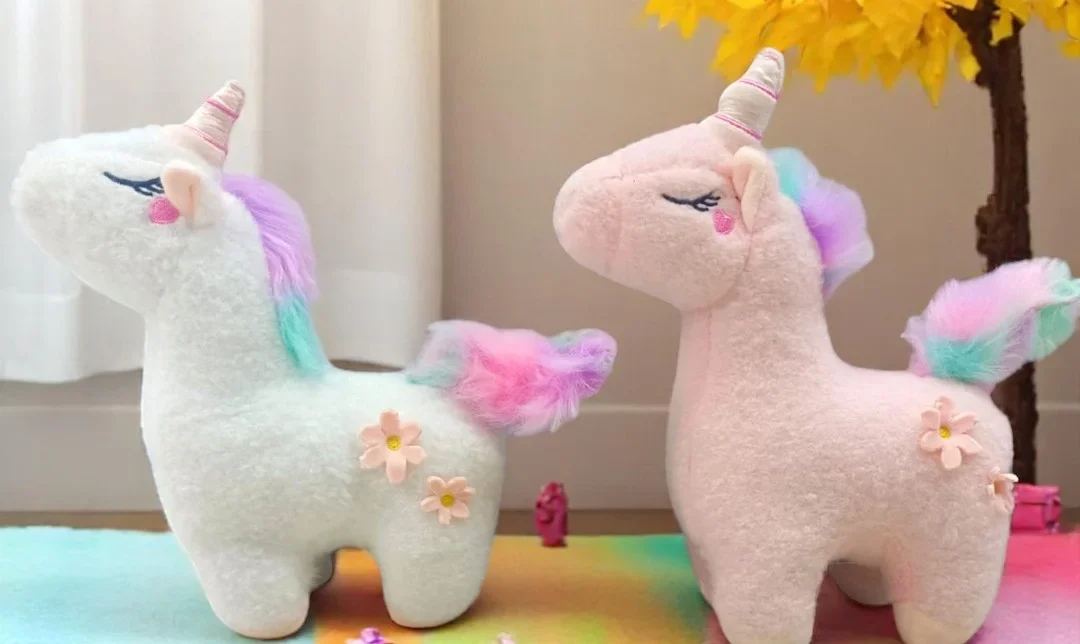 Two adorable unicorn plush toys with rainbow manes and floral details placed on a colourful mat near a bright yellow artificial tree