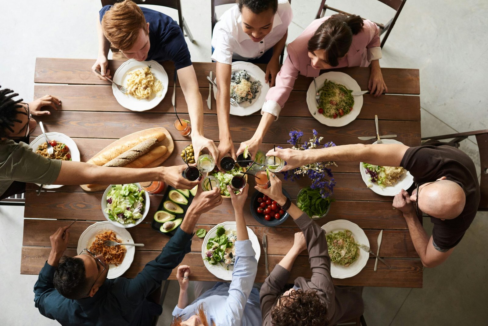 A group of friends seated around a dining table, raising their glasses in a cheerful toast while sharing a meal