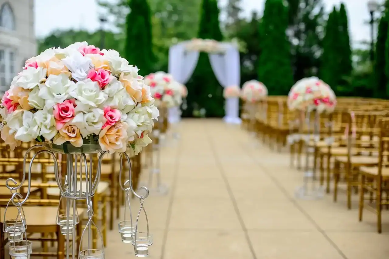 Outdoor wedding aisle decorated with pastel rose flower arrangements and white mandap arch