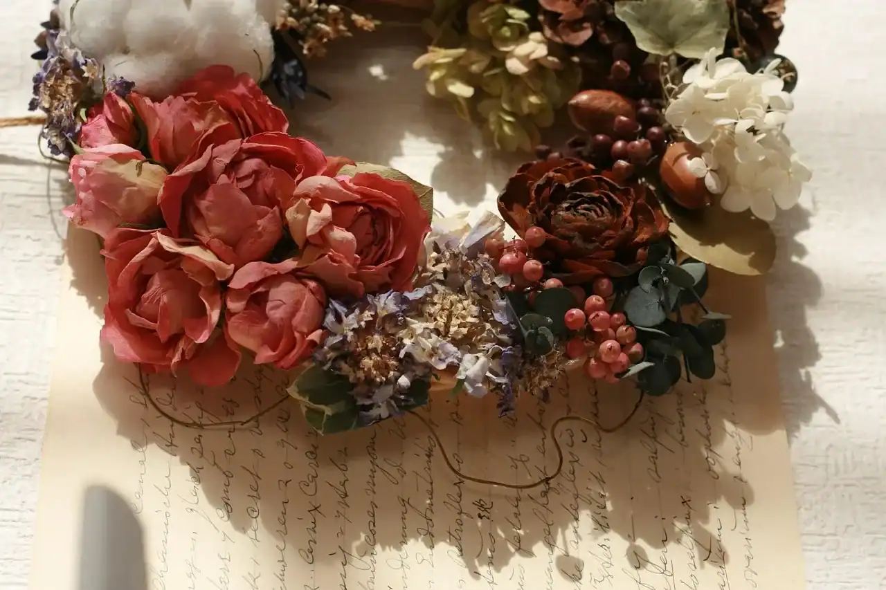 Natural dried flower wreath with preserved roses, cotton, berries, and hydrangea arranged on a rustic background, showcasing elegant dried floral decor.