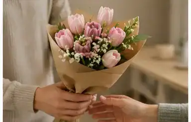 Person gifting a hand-tied pink tulip bouquet wrapped in kraft paper with white baby's breath, fresh spring flower gift for special occasions