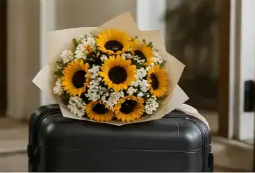 Vibrant sunflower bouquet with baby's breath wrapped in kraft paper resting on a black travel suitcase, perfect flower gift for travelers
