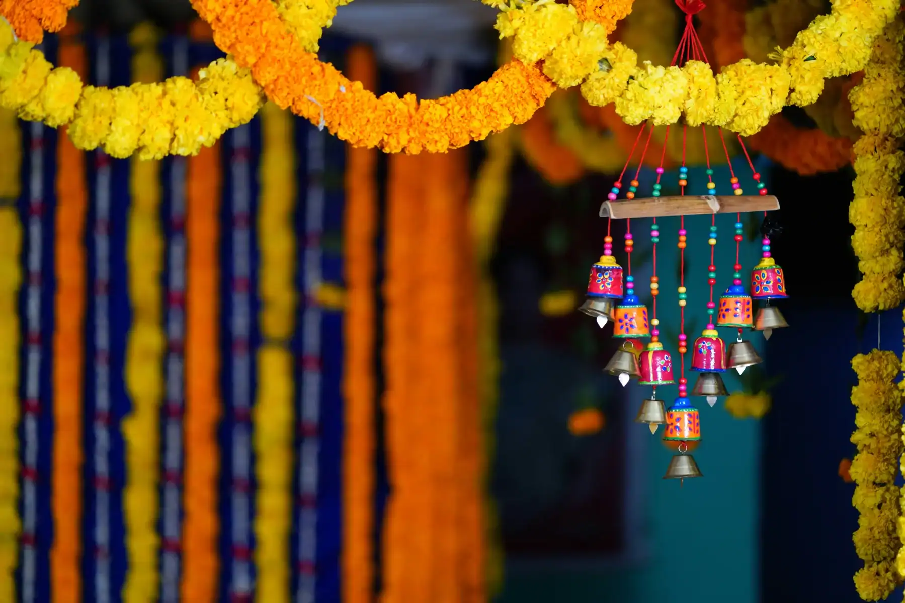Yellow and orange marigold genda phool garlands with colorful hand-painted Indian bell windchime hanging at decorated entrance, traditional Indian festival and wedding door decoration