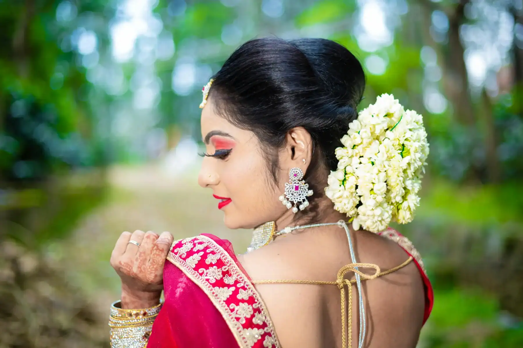 South Indian bride in red silk saree with gold embroidery wearing white jasmine gajra in bridal bun hairstyle and diamond earrings, traditional Indian bridal flower hair decoration