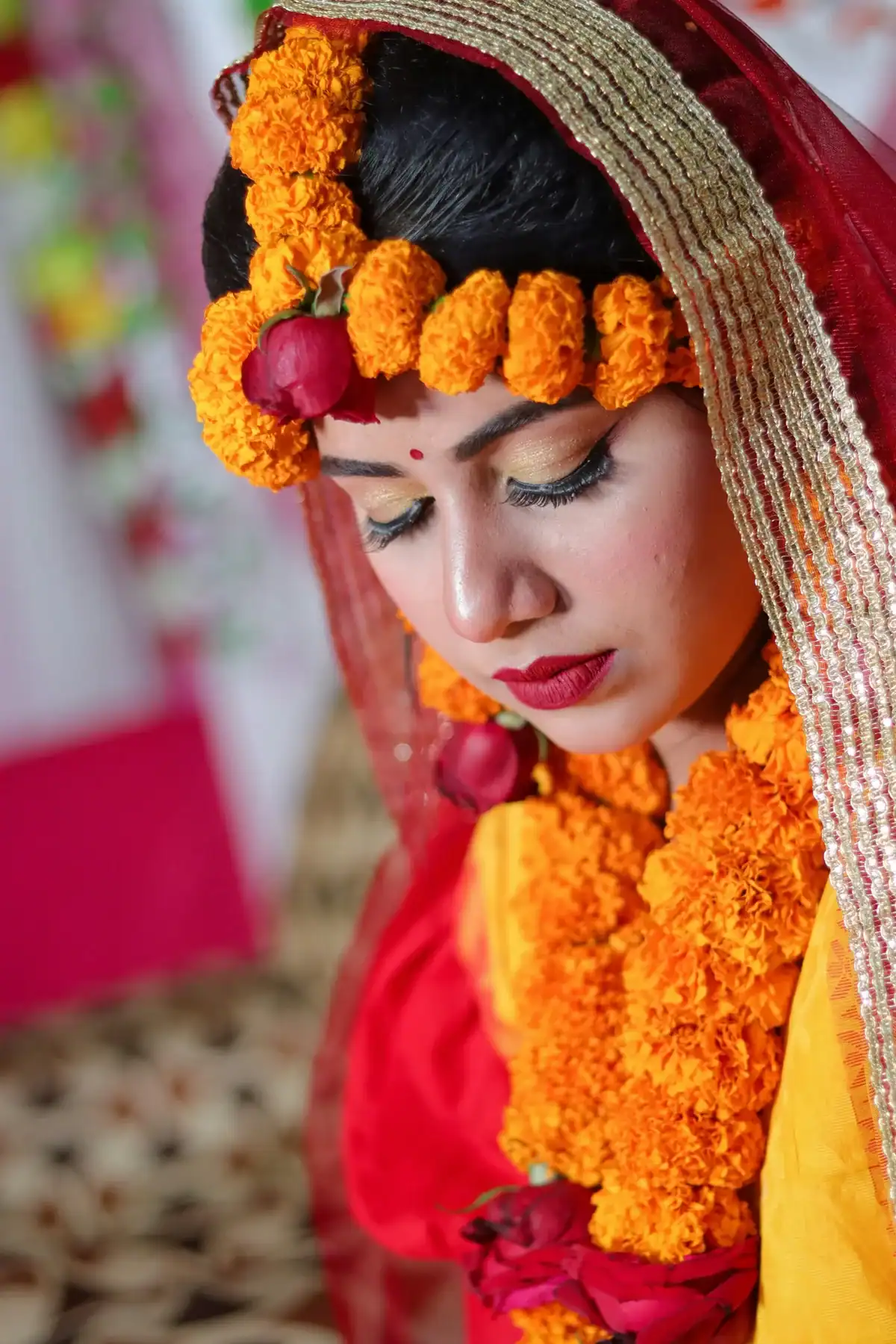 Bengali Indian bride with eyes closed wearing orange marigold genda phool hair garland and matching floral necklace with red veil, traditional Indian bridal flower jewellery